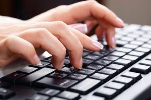 Duas mãos femininas digitando num teclado de computador.